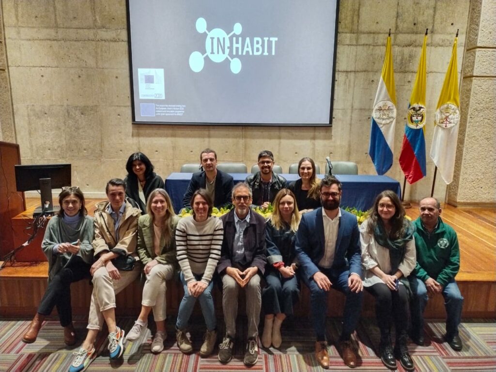 researchers pose for a photo at the Pontificia Universidad Javeriana in front of a screen with the in-habit logo.